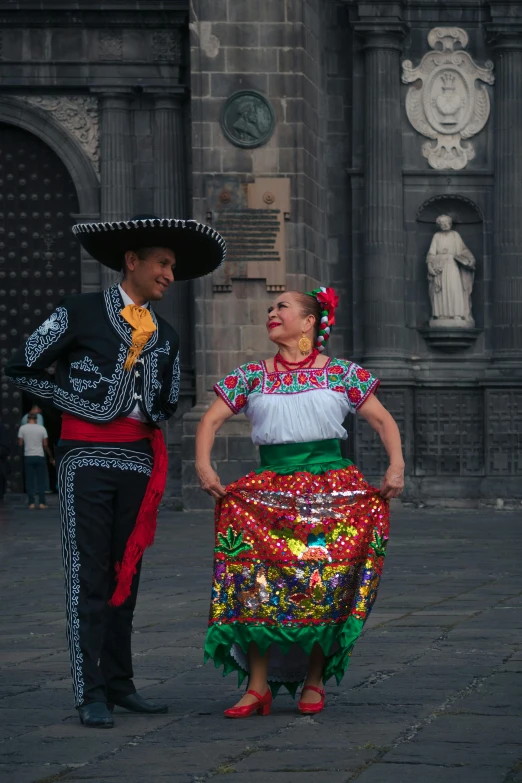 a woman and man in elaborate attire stand next to a wall