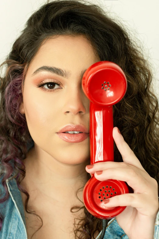 woman holding old style red telephone in one hand and looking at camera