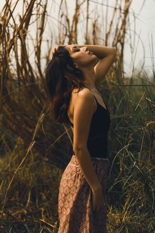 a woman in a floral skirt and high collared top with her eyes closed while holding her head on her hair