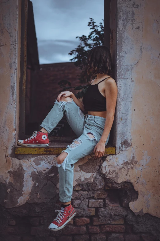 the woman is wearing ripped jeans, black tank top and red tennis shoes