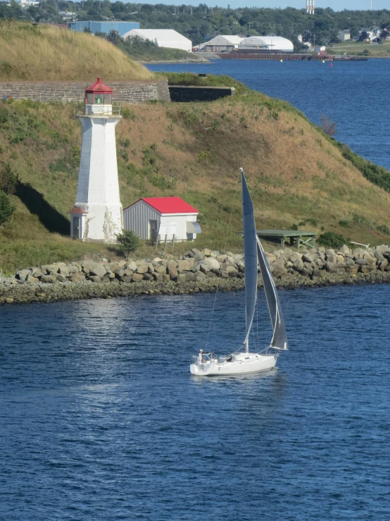 a sail boat in a harbor with a lighthouse in the background