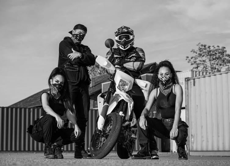 three girls posing with their motorcycle parked by a fence