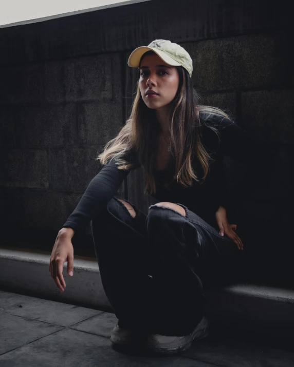 the woman sits on the curb in a baseball cap