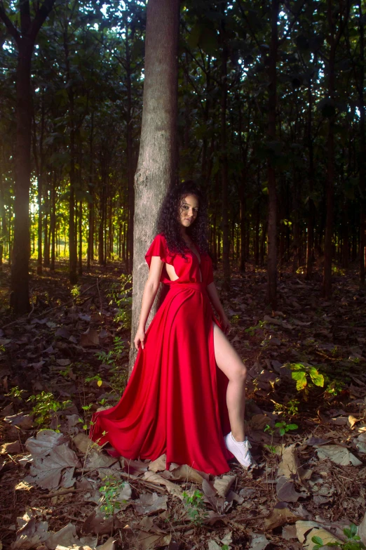 a woman wearing a red long dress standing in the forest