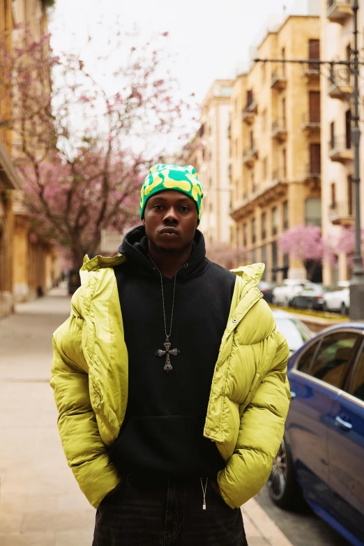 the man in the green coat stands on a sidewalk in front of the blue car