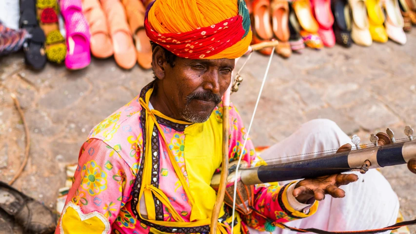 man with orange turban sitting down holding a metal contraption