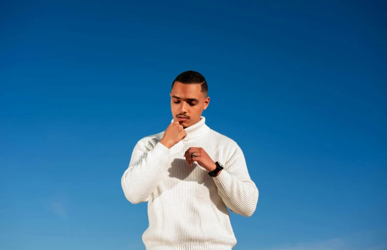 a man in sweater and jeans poses under a blue sky