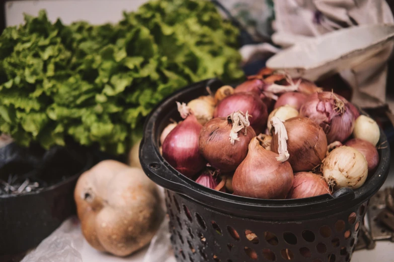 a basket filled with onions next to other vegetables