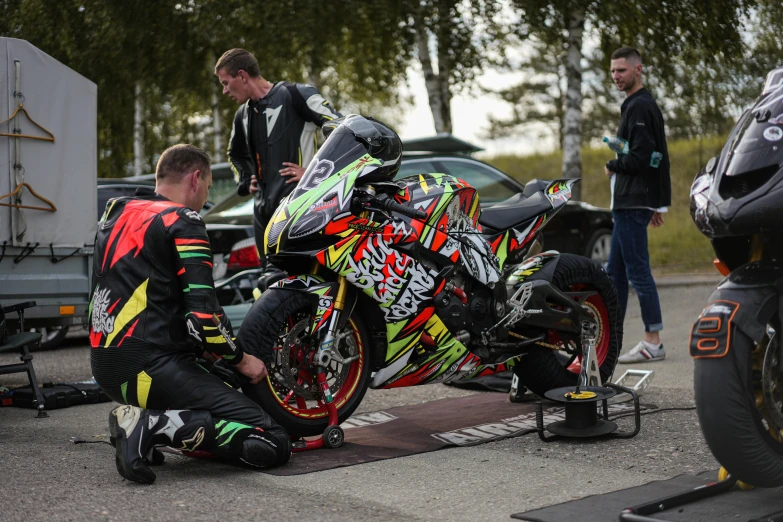 man fixing motor bike on pavement with several others