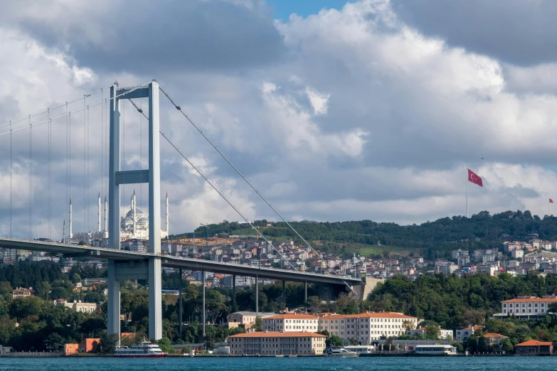 a long suspension bridge across water with houses and city in the background