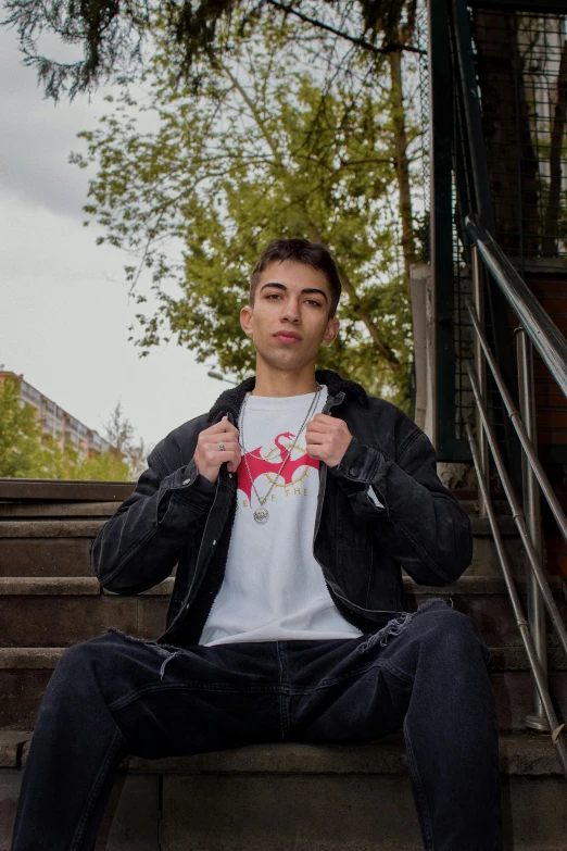 a young man wearing a jacket and pants sitting on steps