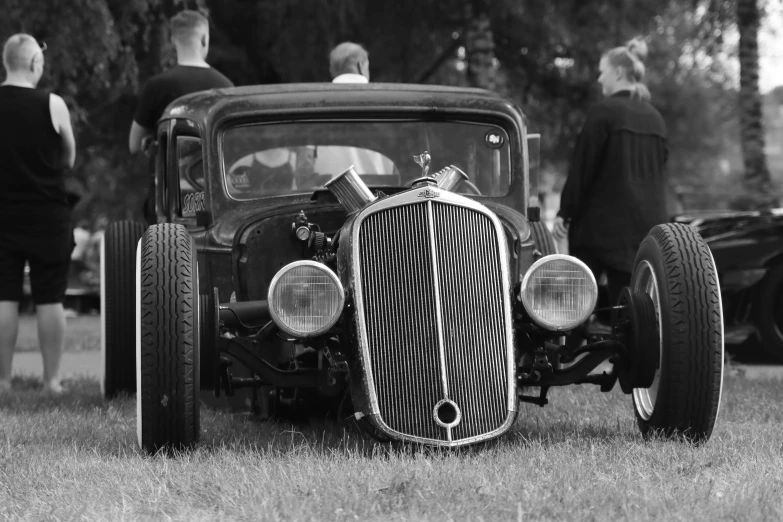 people standing around the front of an old fashioned car