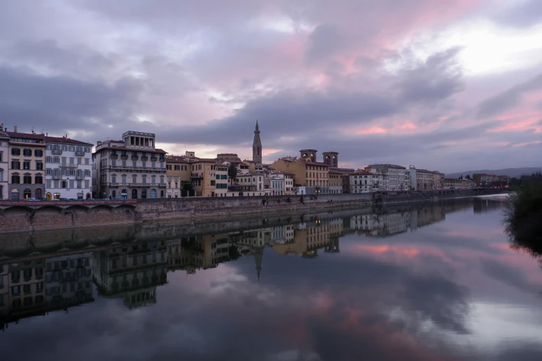 a long, small waterway is lined with buildings and towers under a cloudy sky