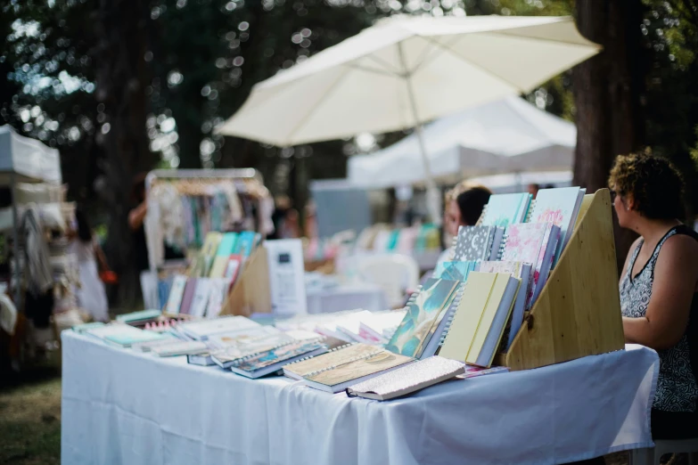 people sitting at a table with many books under umbrellas