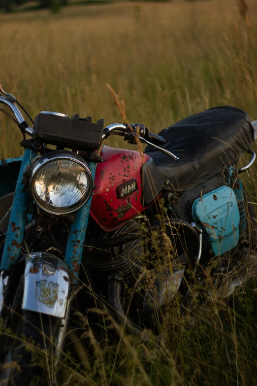 a rusted motorcycle sits on a grassy field