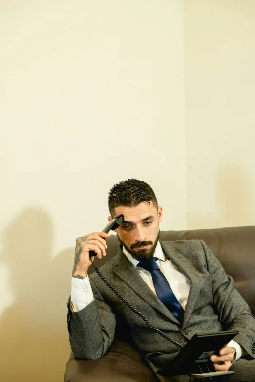 a man in a suit and tie sits on a couch with his hands near his face