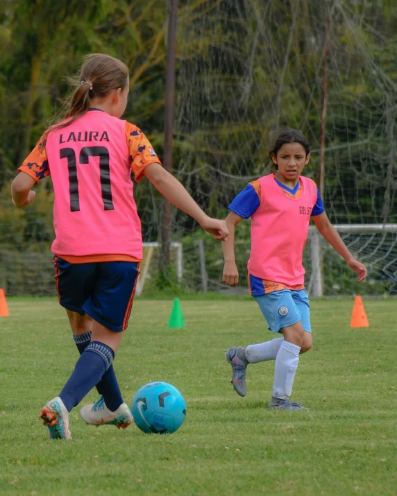 two girls with blue and pink uniforms kicking around a ball