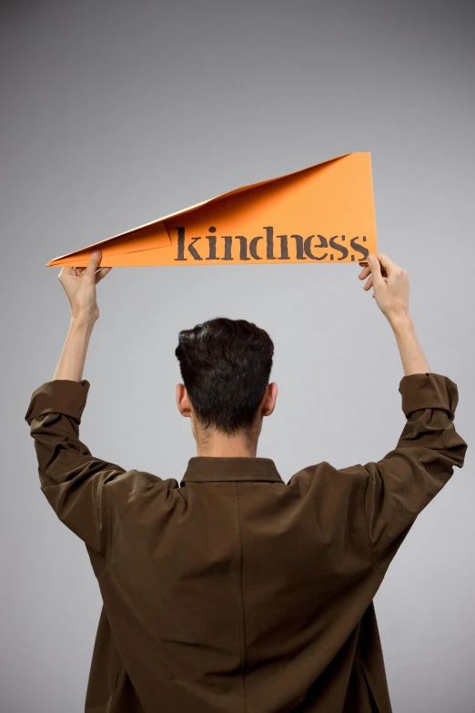 man holding up a yellow paper with the words kindless on it