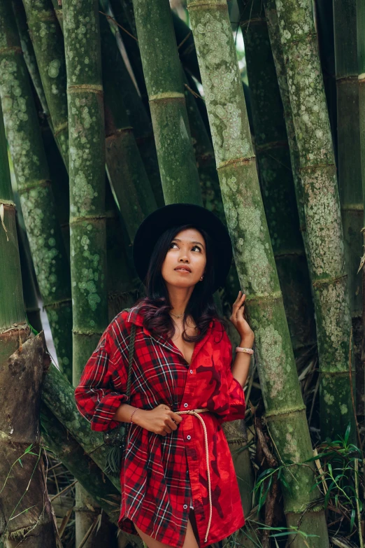 a woman in a hat and red shirt standing near bamboo trees