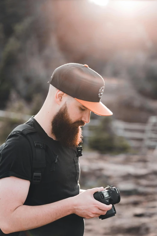 a bearded man with a goatee and hat checking his camera