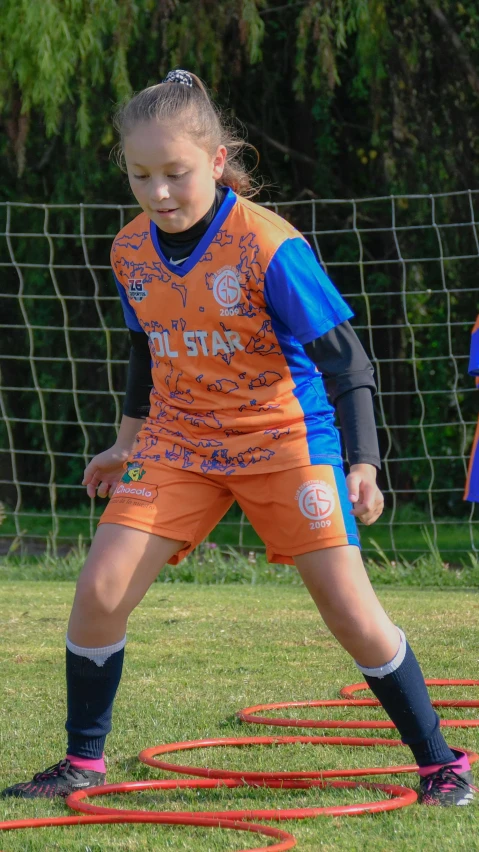 a little girl wearing an orange and blue uniform