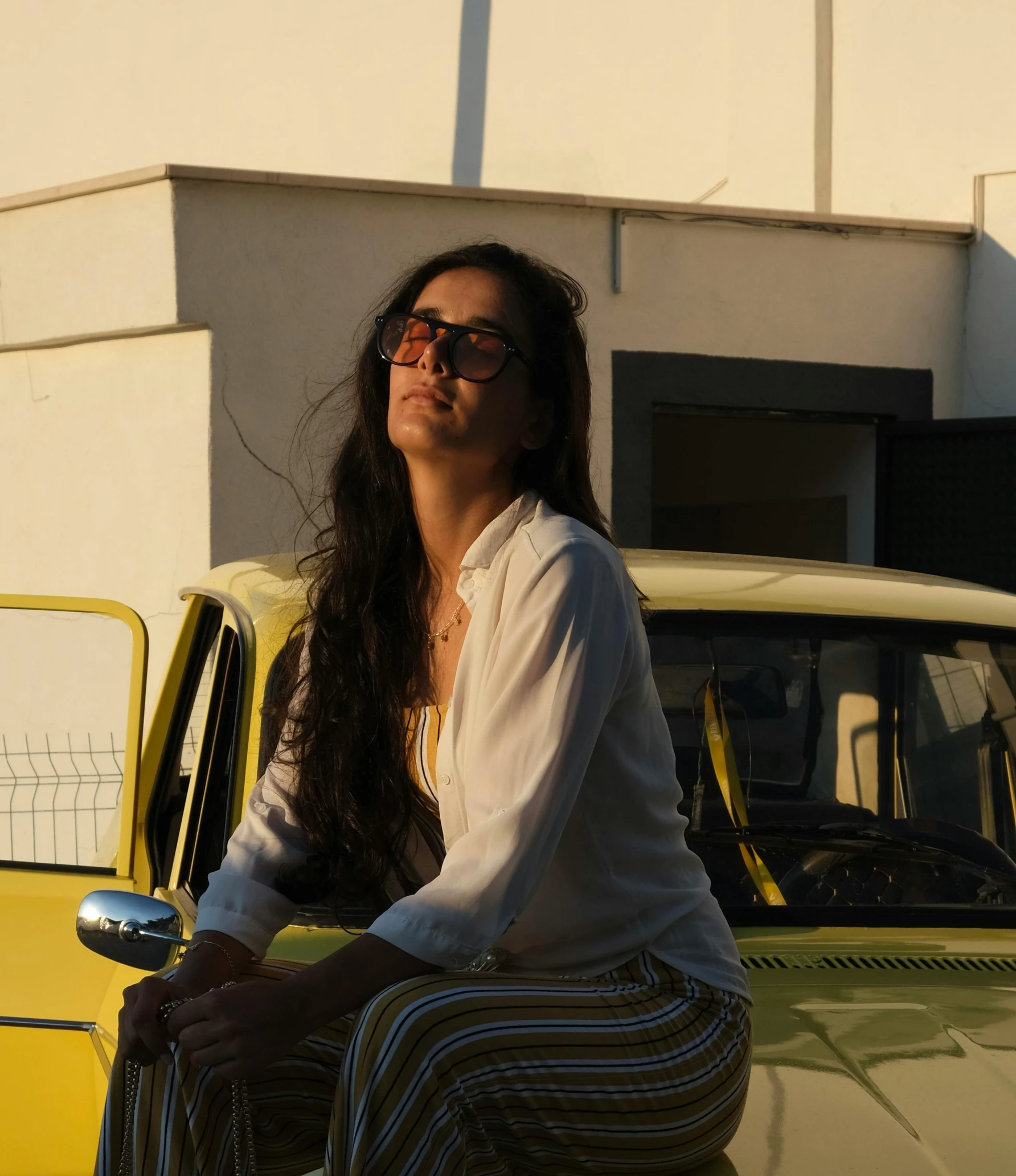 woman with glasses on kneeling on the hood of a car