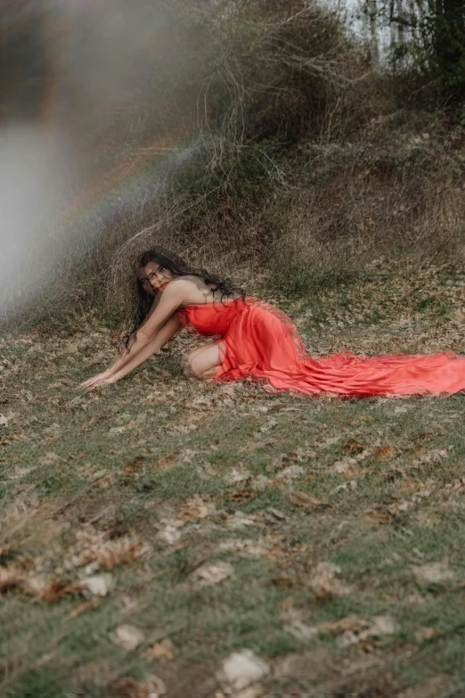 a woman in a red dress laying on the grass in the fall