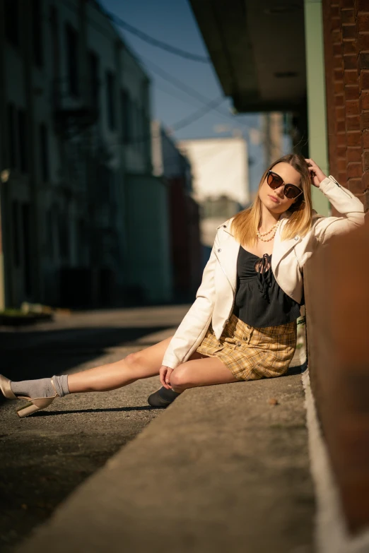 a woman in dress and sunglasses sitting on the sidewalk