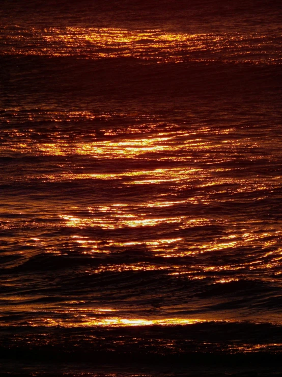 a plane flying over some ocean waves at sunset