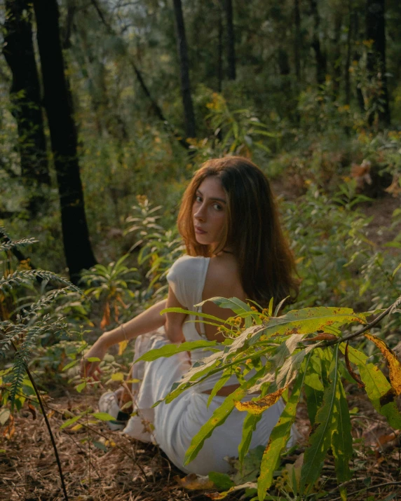 woman wearing white sitting in forest looking at camera