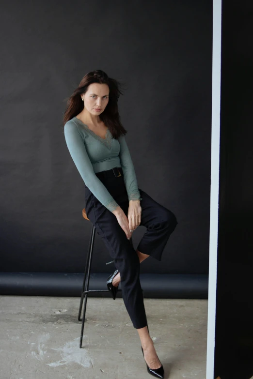 young woman wearing black trousers and green shirt posing on chair