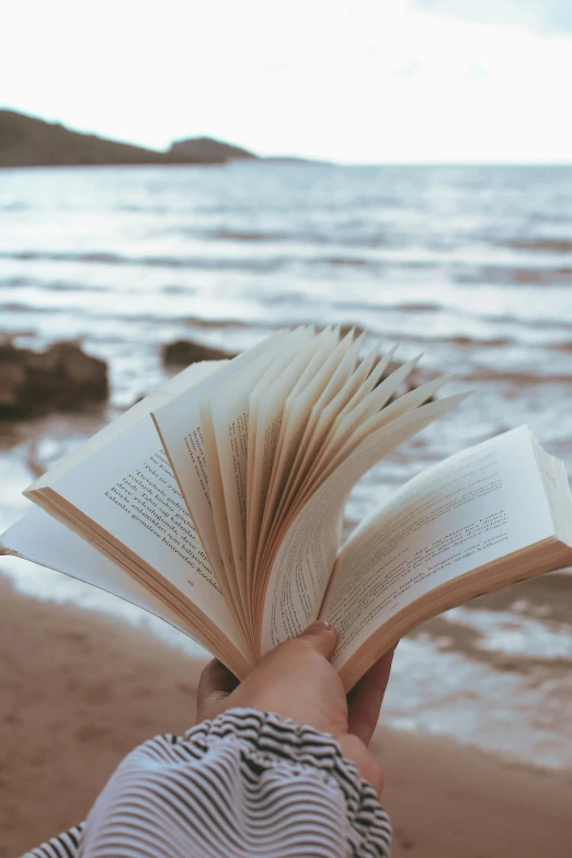 a person is reading a book while sitting at the edge of the water