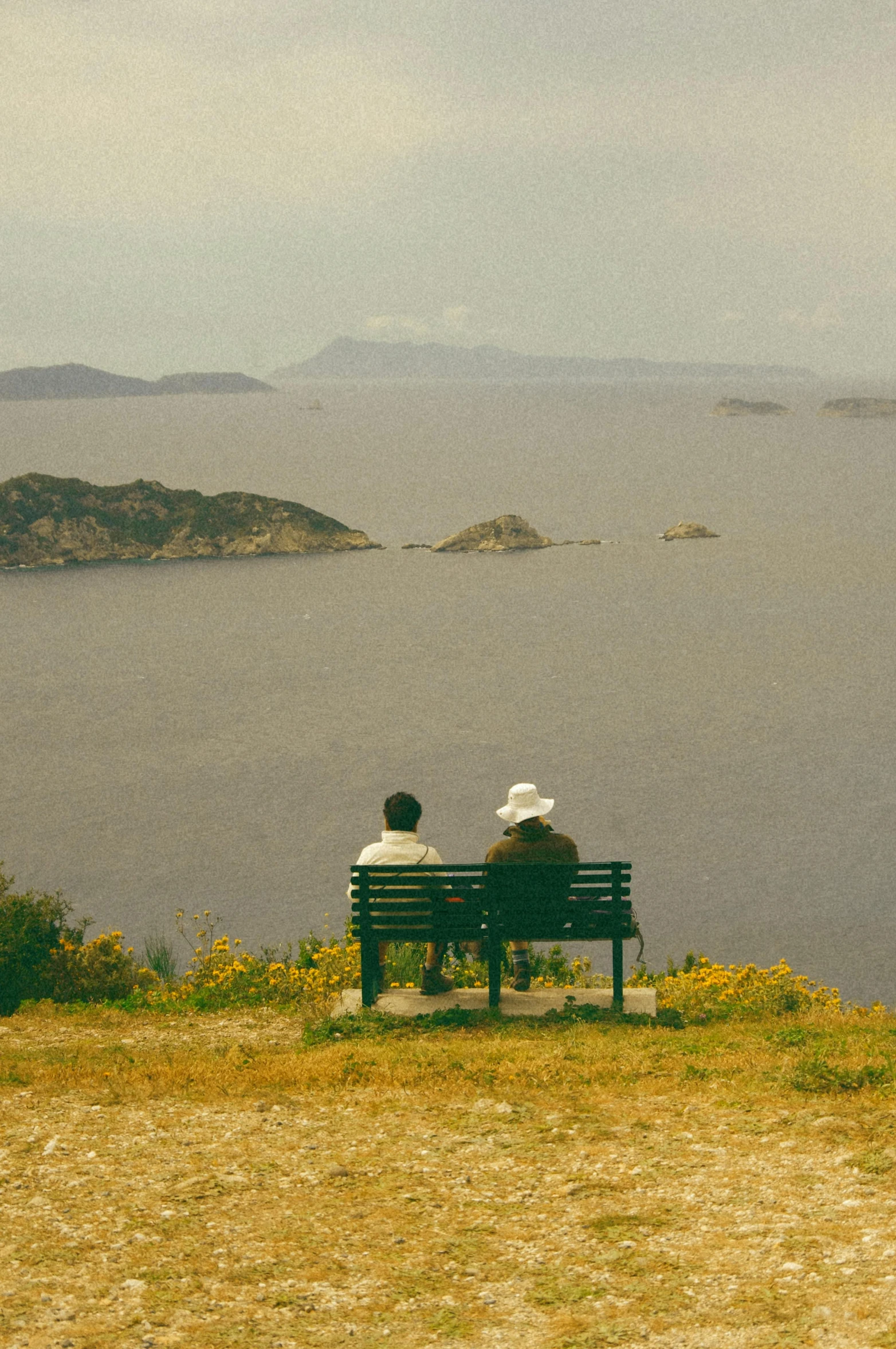 two people are sitting on a bench overlooking the ocean