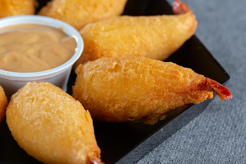 several fried foods are on a black tray next to dipping sauce