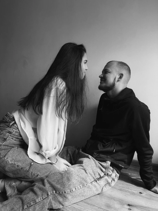 a man and woman sitting on the ground in front of a wall