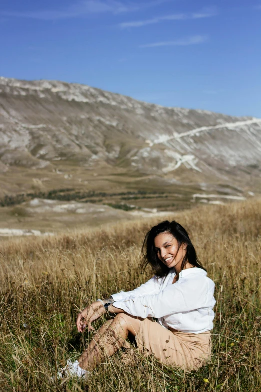 the woman is sitting on the hill wearing a white shirt