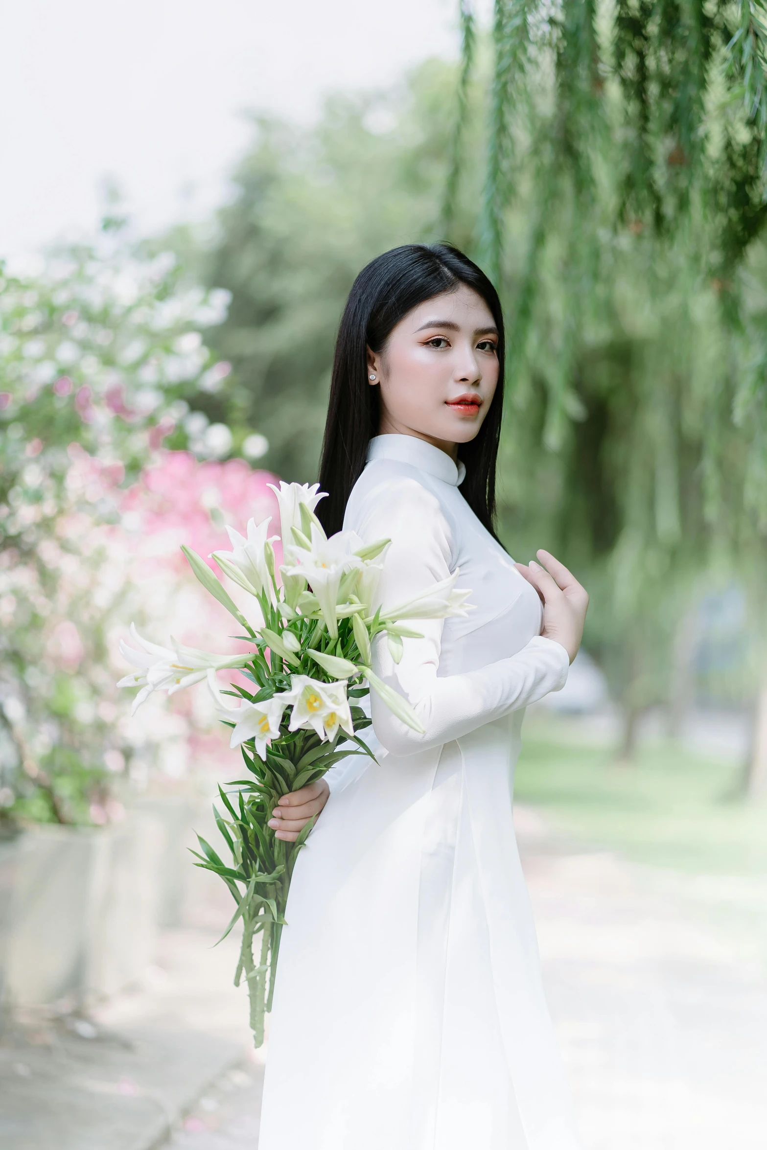 a woman standing next to flowers holding a white bouquet