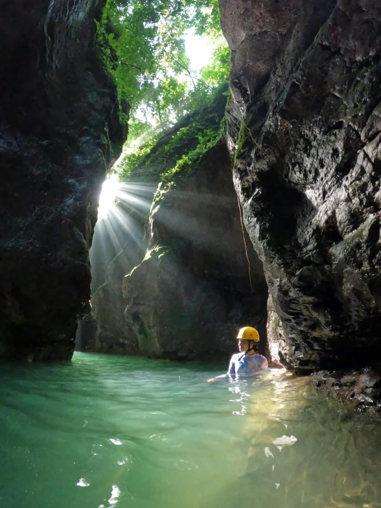 a man with a yellow hat wading in water near large cliffs