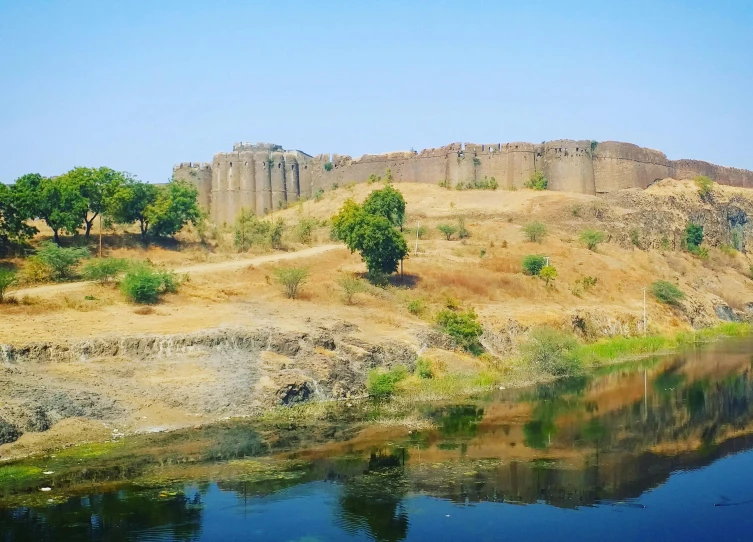 an arid cliff with some trees near water