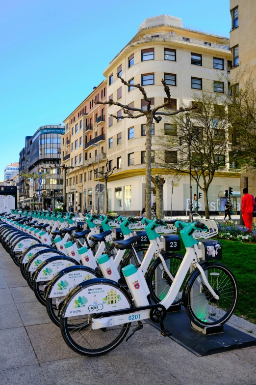 a large row of bikes parked near a curb with buildings in the background