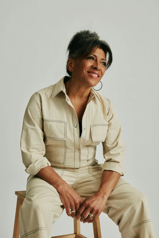 woman wearing white pants sits on a stool smiling