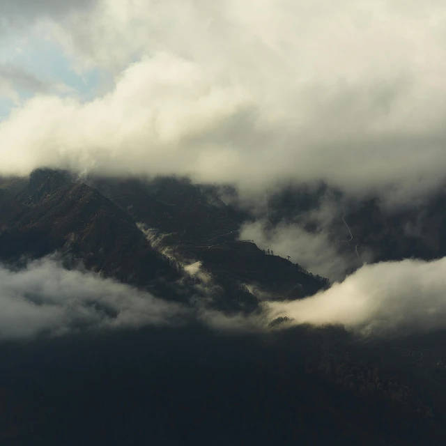 a mountain covered with clouds with a lone bird flying overhead