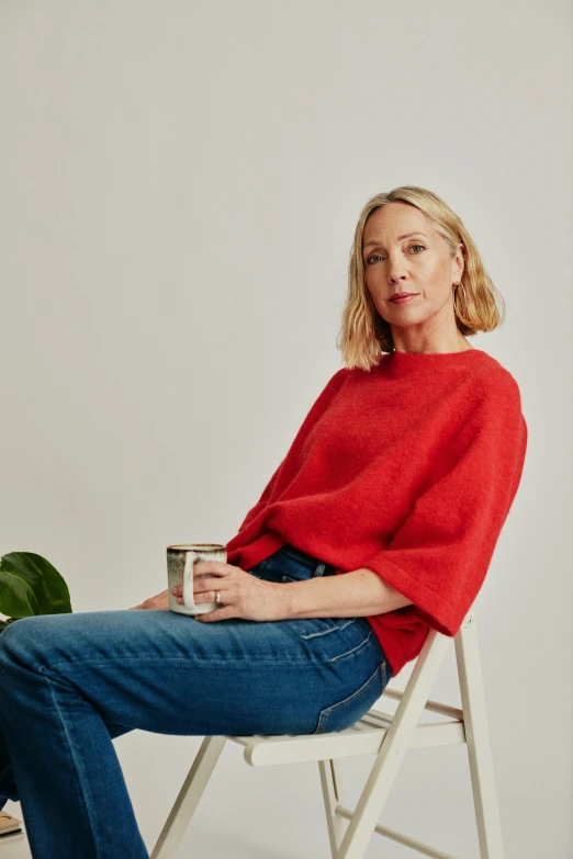 a woman in red sweater sitting on chair with cup