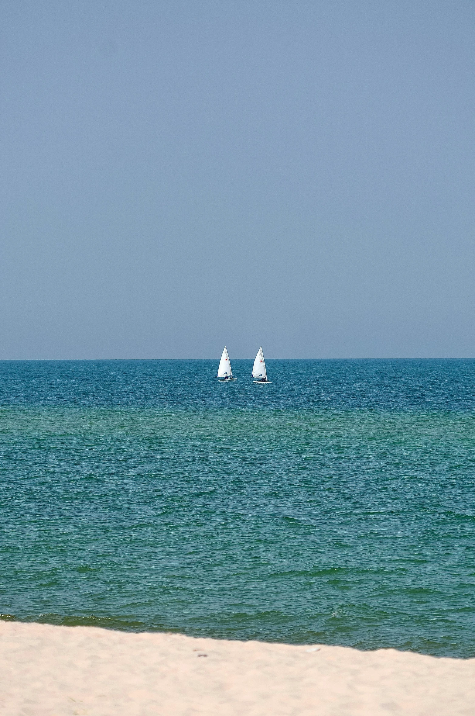 a sandy beach has a small sailboat out in the ocean