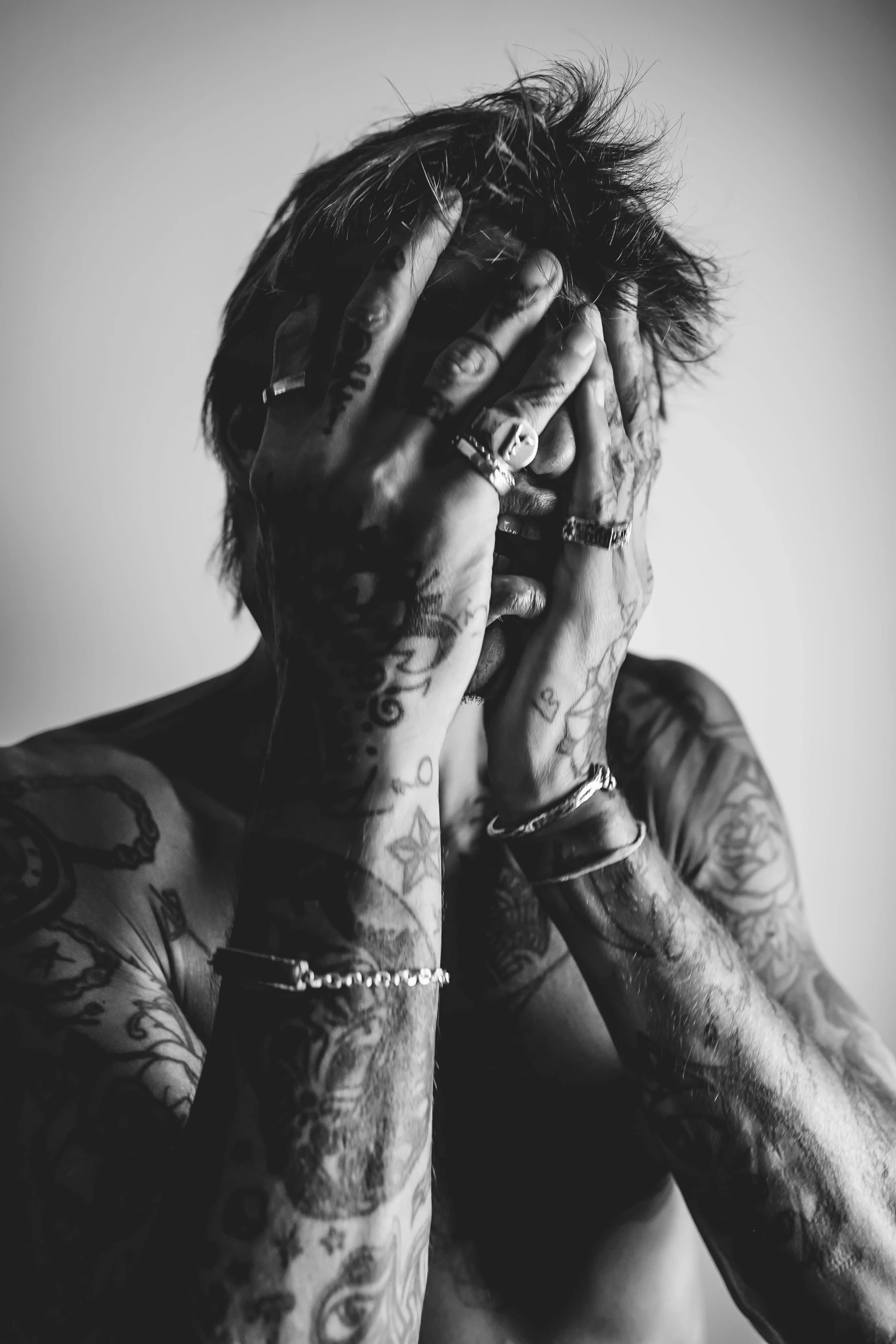 a man with tattoos covers his face with his hands