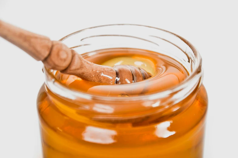 a honey in a glass jar with a wooden spoon inside