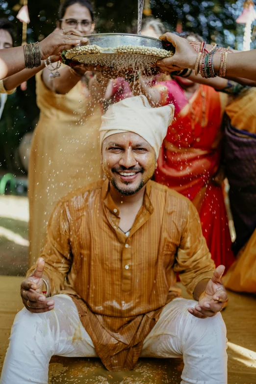 man with an indian headgear on sitting under water pouring from bowl