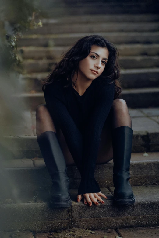 a woman sits on stairs in boots with one foot resting