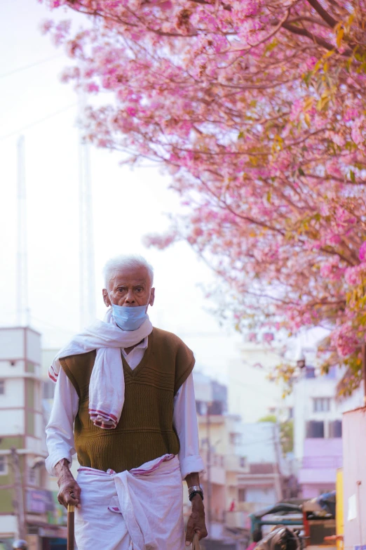 man with face mask standing near cherry blossoms