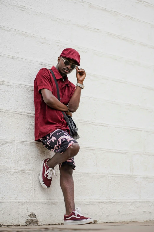 a man leaning against a wall wearing red shoes